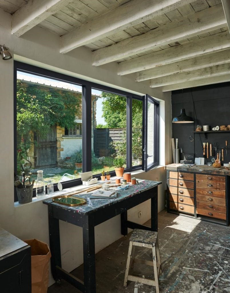 Fenêtre noir ouverte dans un atelier de peinture donnant sur un jardin